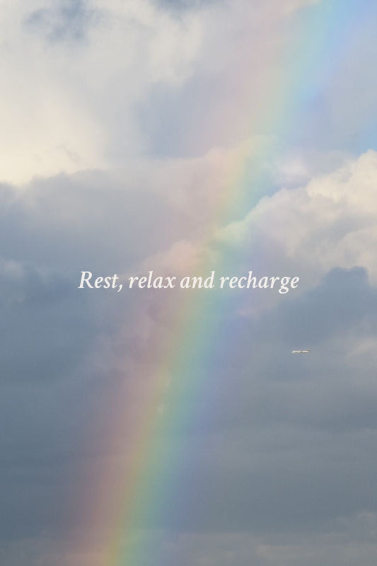 A vibrant rainbow stretches across a cloudy sky after rain, with soft text overlay reading ‘Rest, relax and recharge’ on a peaceful blue-gray background, inspiring calm and renewal.